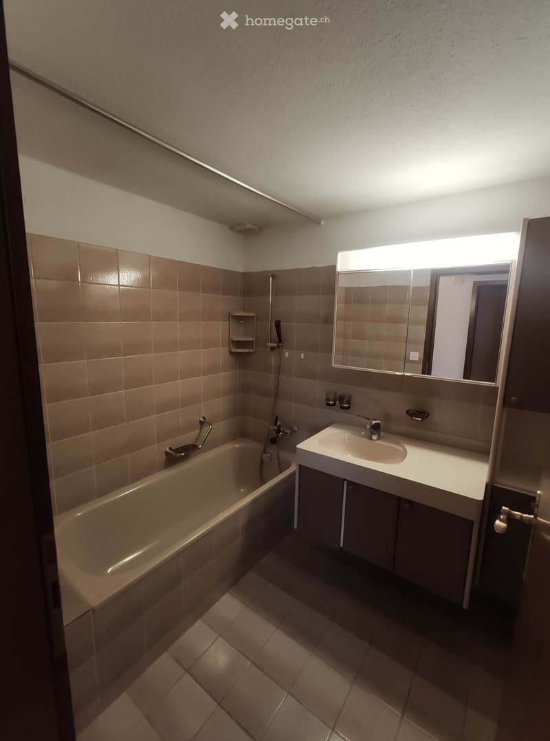Modern bathroom with beige tiles, a bathtub, a sink with a mirror, and a showerhead.
