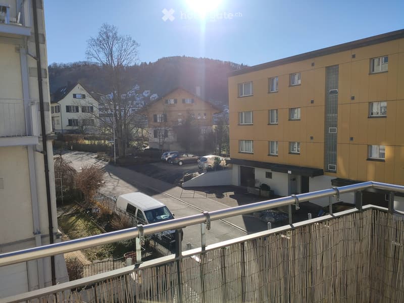 Balcony overlooking a residential area with parked cars, buildings, and a clear blue sky.
