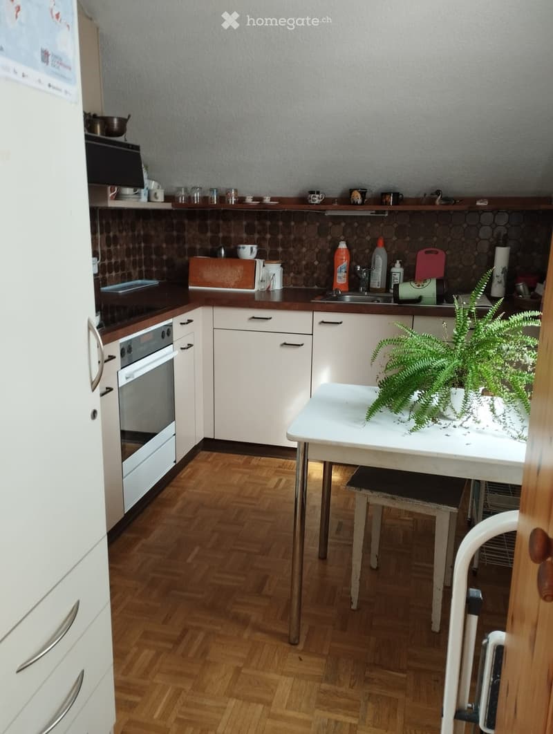 Modern kitchen with white cabinets, wooden countertops, and a small dining area featuring a table and chairs. Includes an oven, sink, and various kitchen items on the counter.