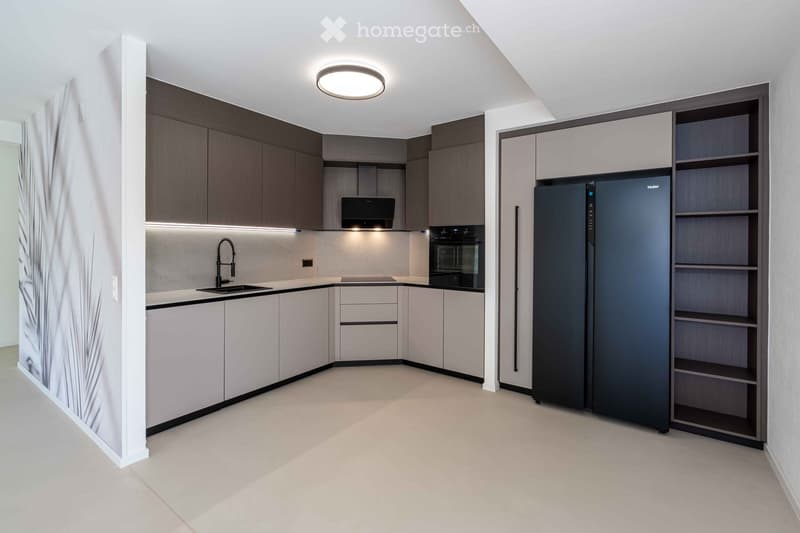 Modern kitchen with sleek, dark wood cabinets, white countertops, built-in oven, refrigerator, and a sink with a modern faucet.