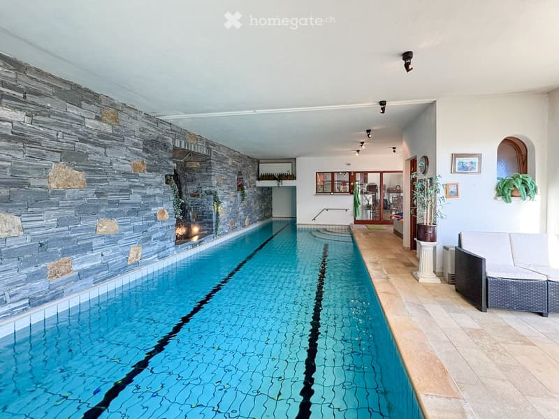 Large indoor swimming pool, with blue tiles and black lines, decorative fireplace on one wall, stone and wooden accents