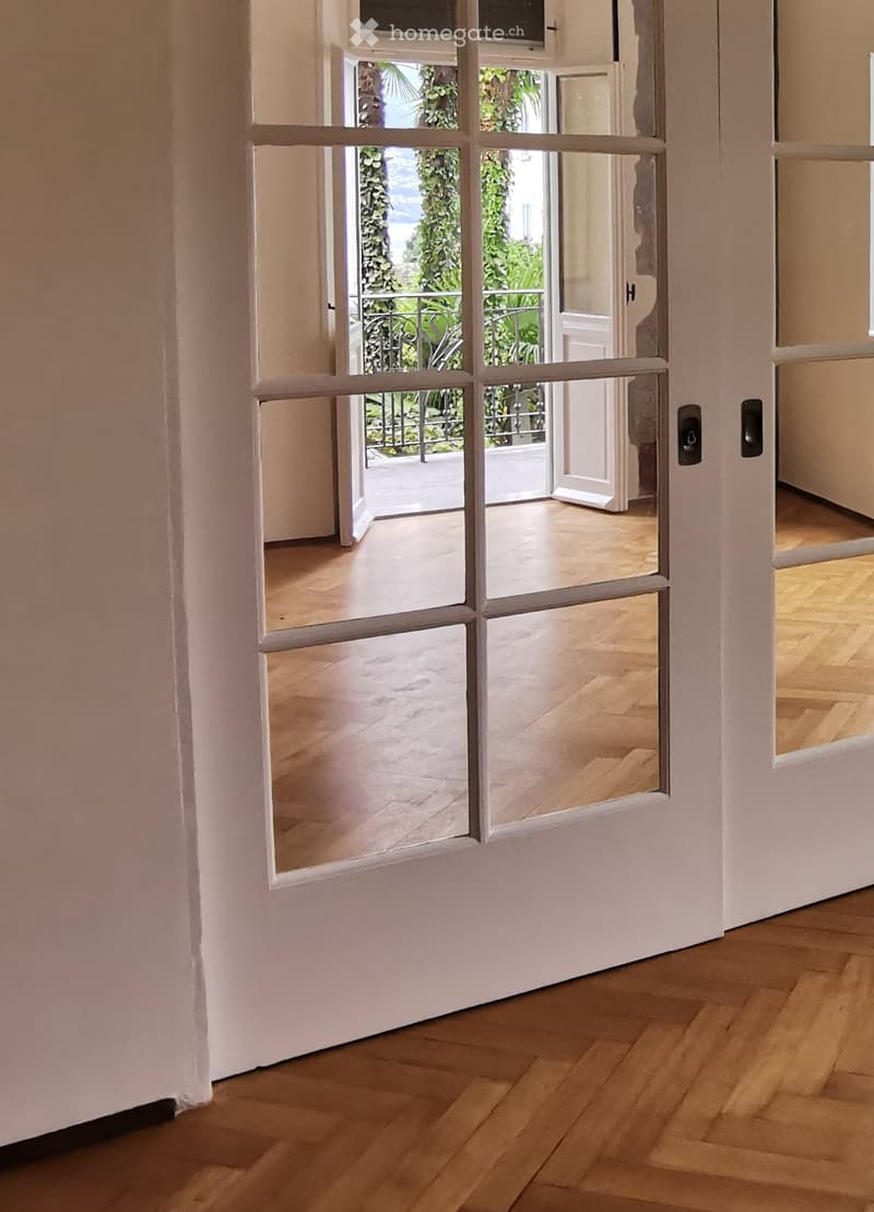 Open sliding glass door leading to a balcony with wooden flooring and white walls.