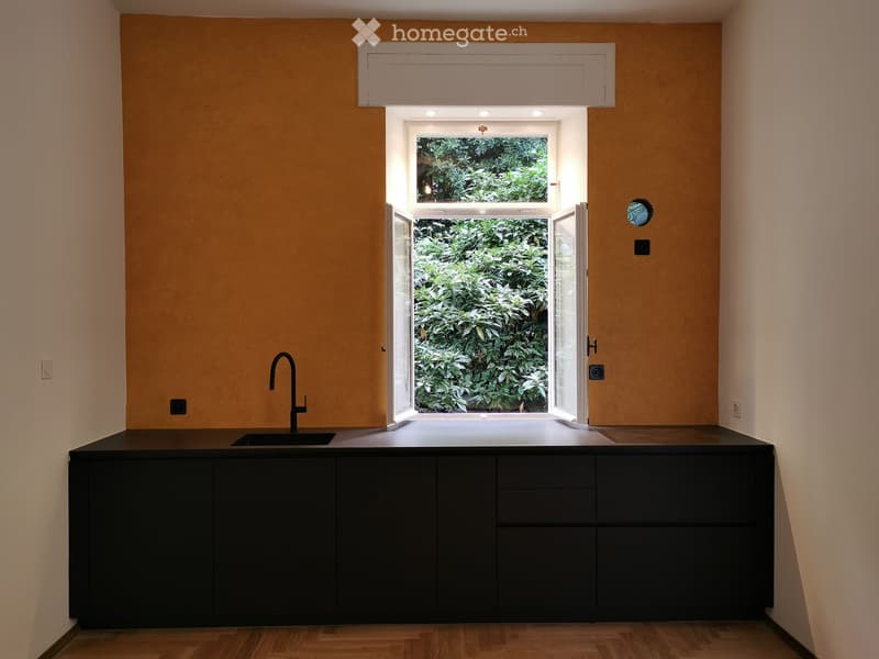 Modern kitchen with dark cabinets, a black countertop, and a sleek faucet, featuring a large window with a view of greenery.