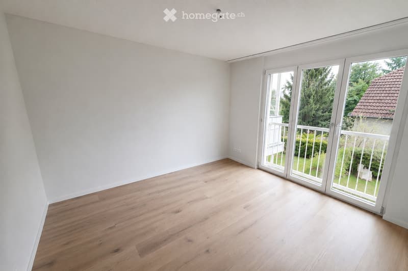 Empty room with light wooden flooring and white walls, featuring large sliding glass doors leading to a balcony or outdoor area.