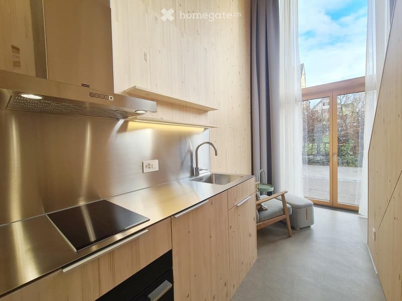 Modern kitchen with wooden cabinets, stainless steel countertops, induction hob, stainless steel sink with faucet, and sliding glass doors leading to a terrace with a view