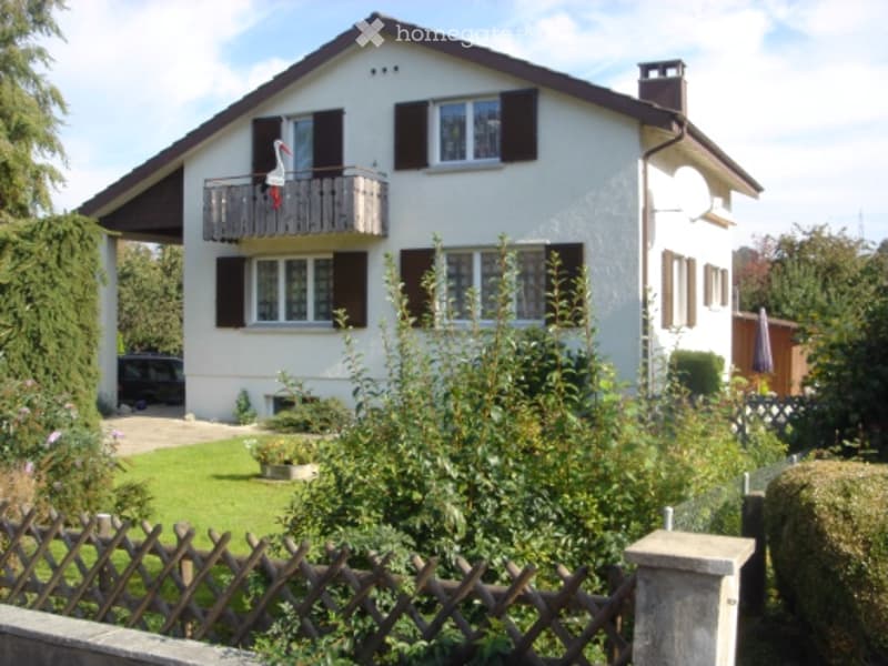 House. Two-story white house with black shutters, balcony, and surrounding garden.
