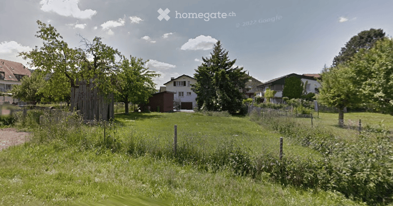 Garden / Outdoor Area. A grassy field with trees and a few houses in the background, surrounded by a wooden fence.