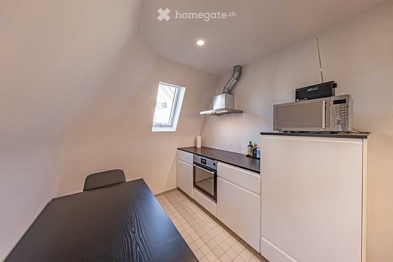 Modern kitchen with tiled floor, white cabinets, black countertop, stove, microwave, and dining table.