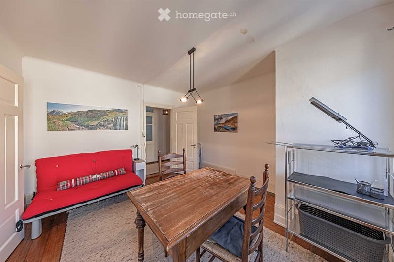 A wooden sofa with pillows, wooden table, chairs, a rug, and decorative paintings.