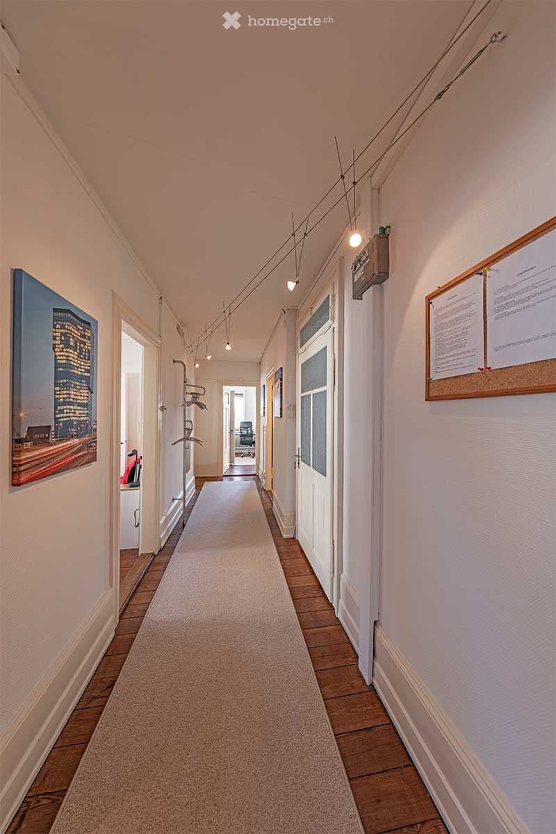 White walls, wooden floor, carpeted hallway, overhead lighting, coat rack, doorways, framed artwork on wall