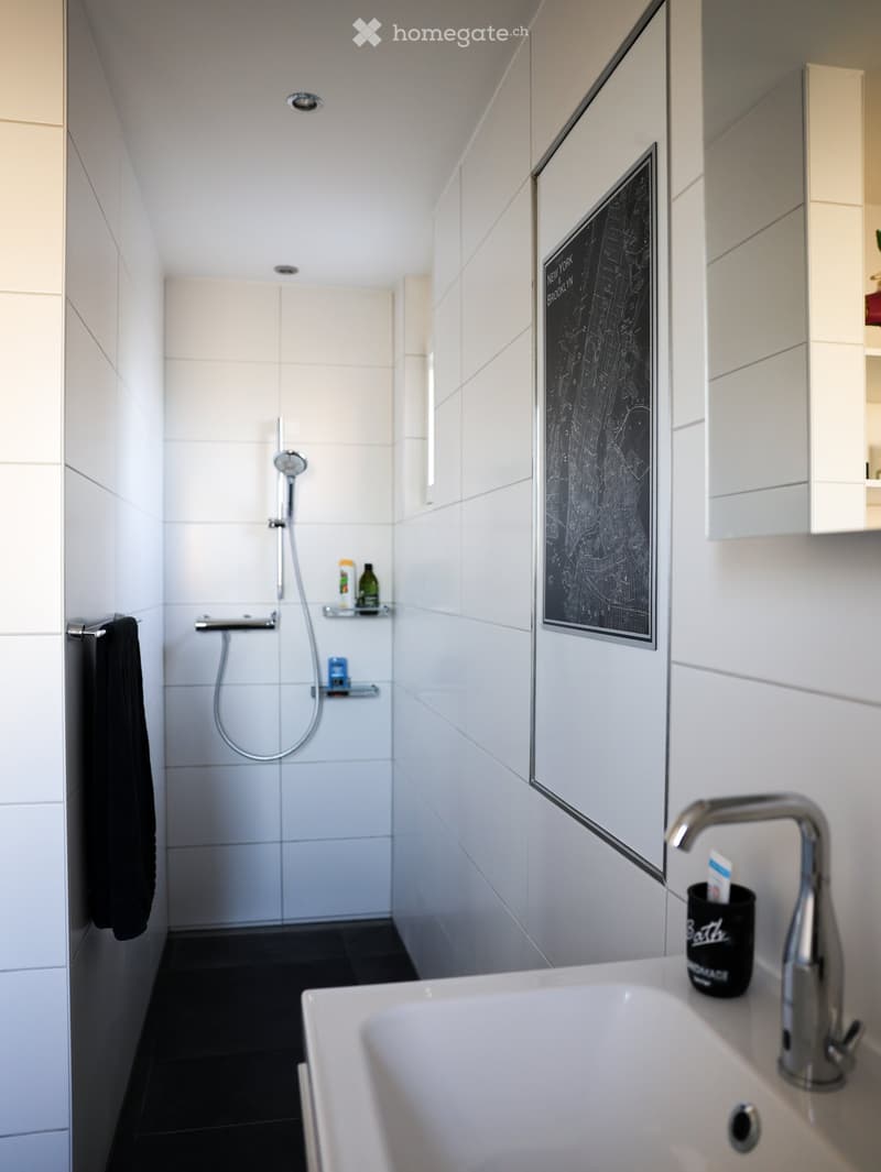 Modern bathroom with white tiles, a large mirror, a shower area, a sink with a modern faucet, and a framed map on the wall.