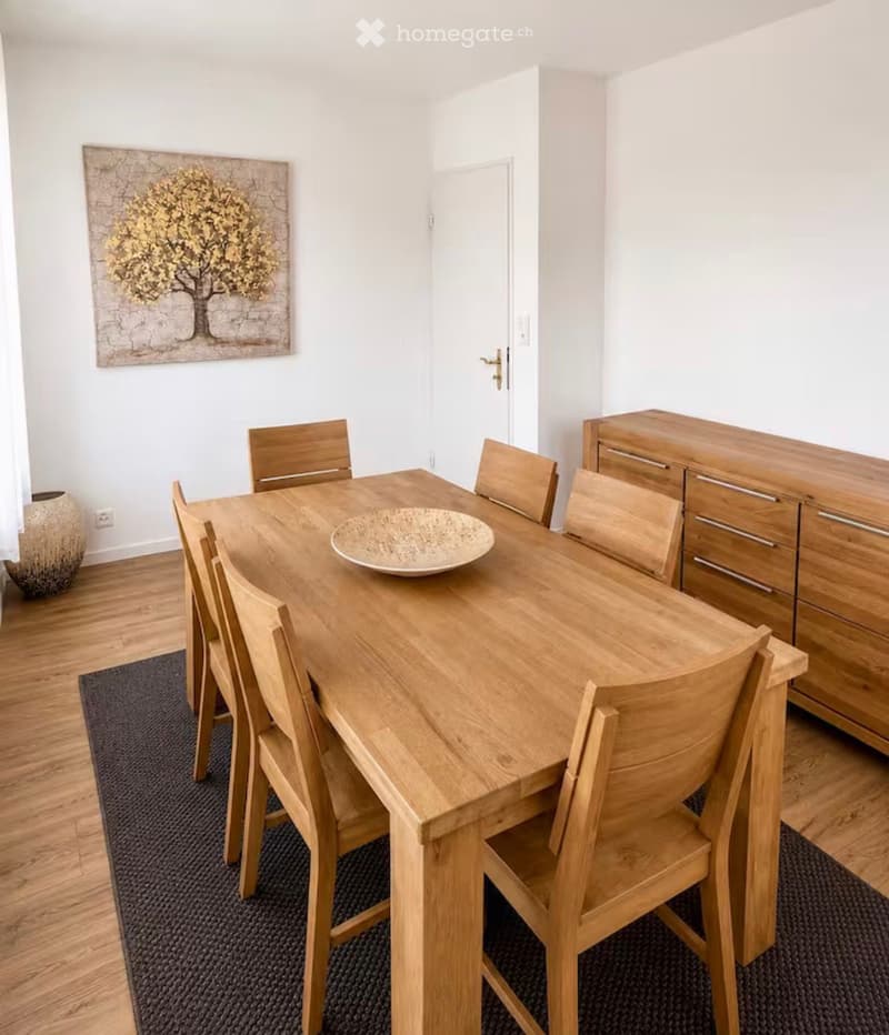 Dining room with a wooden dining table, six wooden chairs, a wooden cabinet, a decorative bowl on the table, and a vase on the floor.