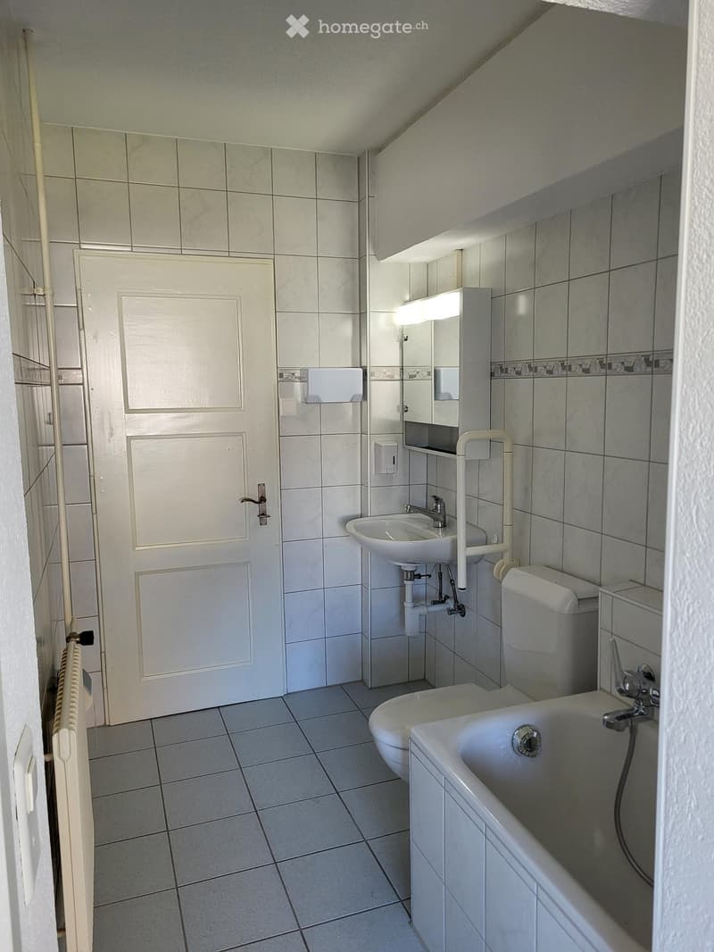 Bathroom with tiled walls and floor, featuring a bathtub, toilet, sink, mirror, and a door.