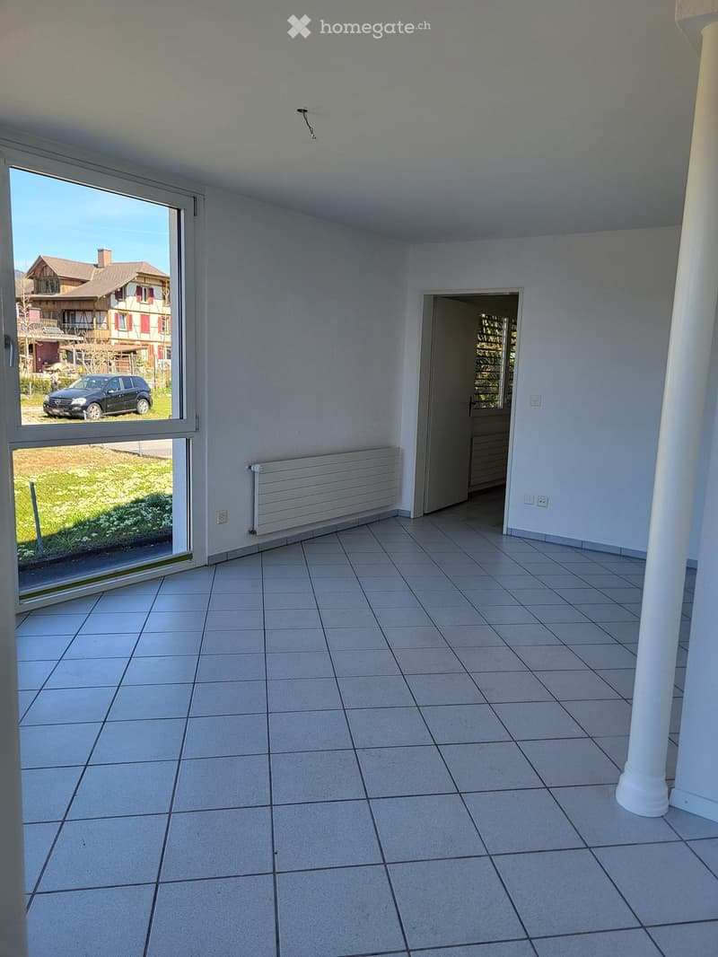 Empty room with tiled floor, white walls, large window, radiator, and a doorway leading to another space.