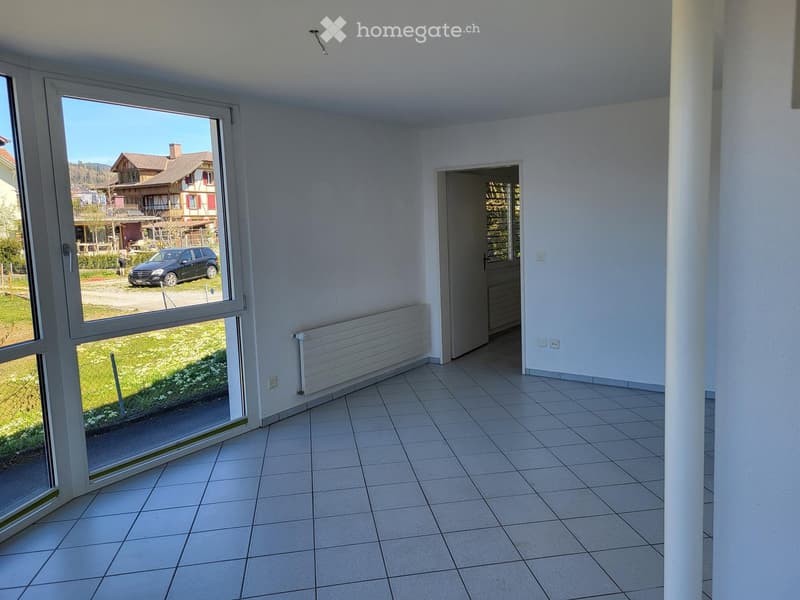 Empty room with tiled floor, large window, radiator, and a door leading to another space.