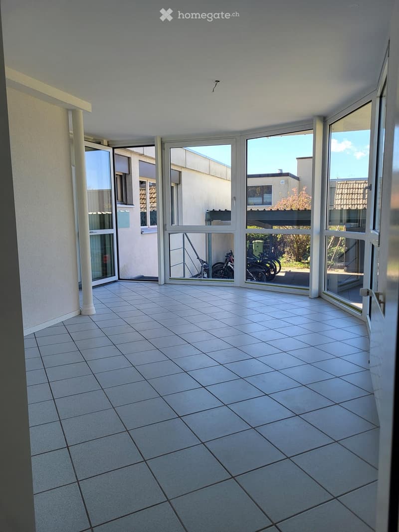 Empty balcony with white tiled flooring, large glass sliding doors, and a view of neighboring buildings and bicycles.
