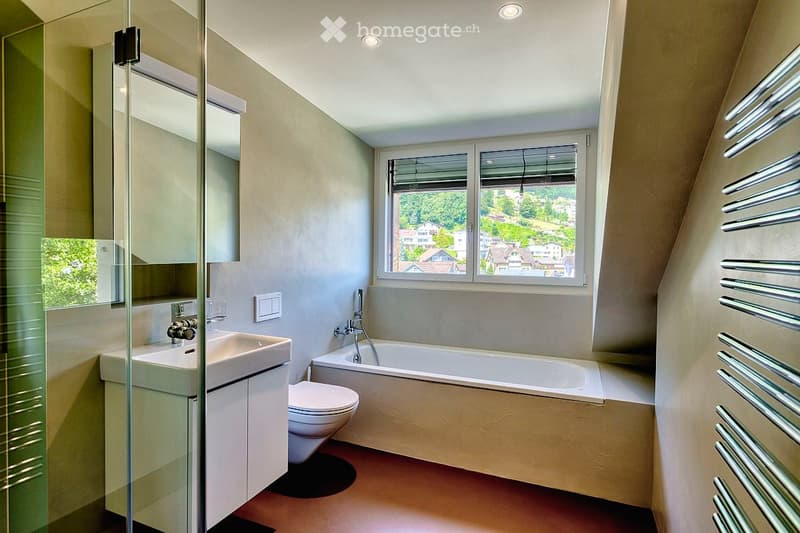 Modern bathroom with a large window offering a scenic view, featuring a sink, toilet, bathtub, mirror, and radiator.