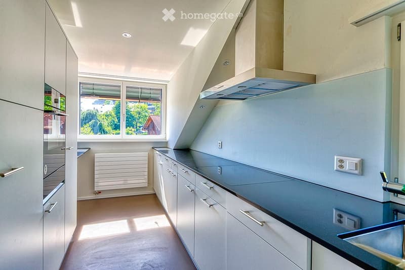 Modern kitchen with white cabinets, stainless steel sink, and a large window offering a view of greenery outside.