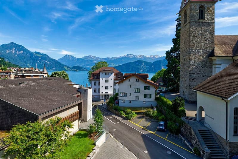 Aerial view of a town with a mix of residential and historic buildings, surrounded by mountains and a lake.