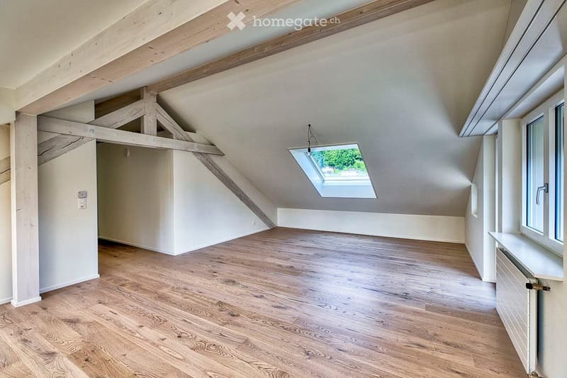 Empty attic room with wooden flooring, exposed wooden beams, and a skylight window bringing in natural light.