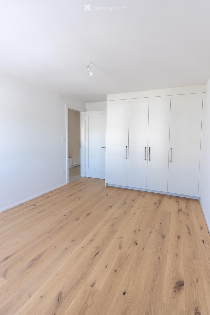 Empty room with light wooden flooring and white walls, featuring built-in white closet units and a visible doorway leading to another room.