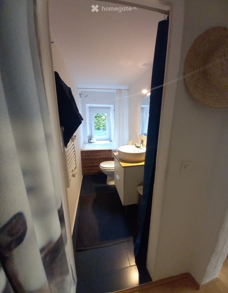 Modern bathroom with a sink, toilet, bathtub, and mirror. The space features a window with a view of greenery outside.