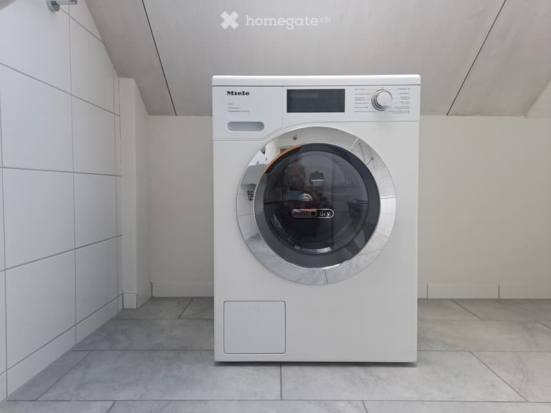 Modern bathroom with a white Miele washing machine featuring a digital control panel and a large transparent door.