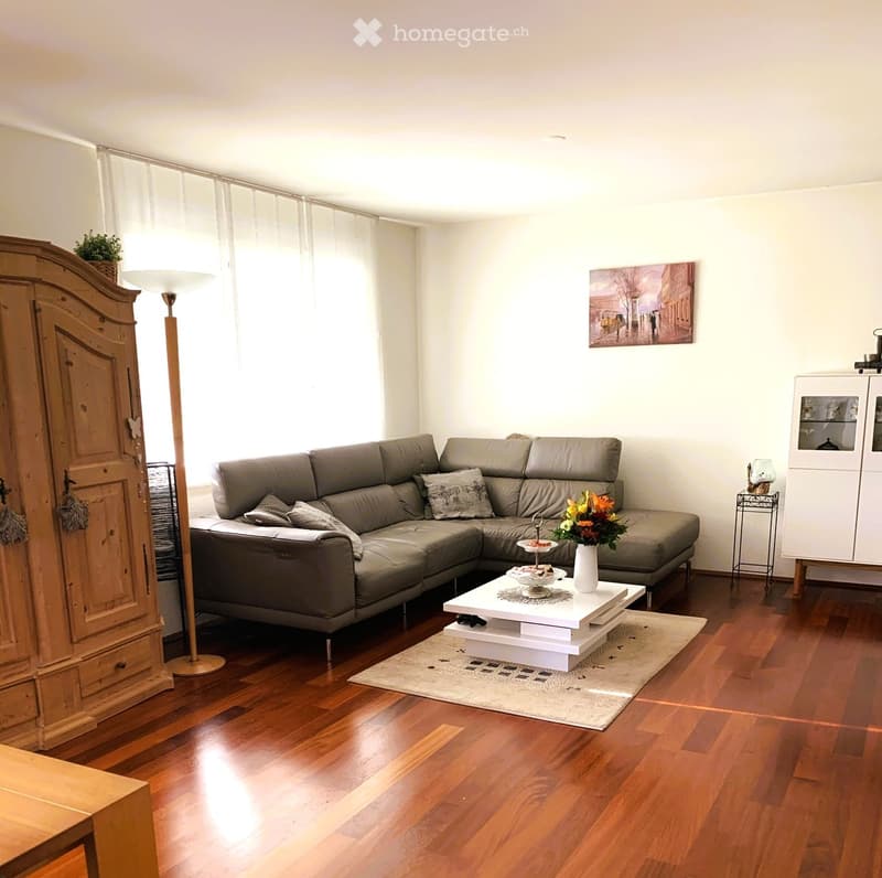 Modern living room with a grey sectional sofa, white coffee table, floor lamp, and wooden cabinet.