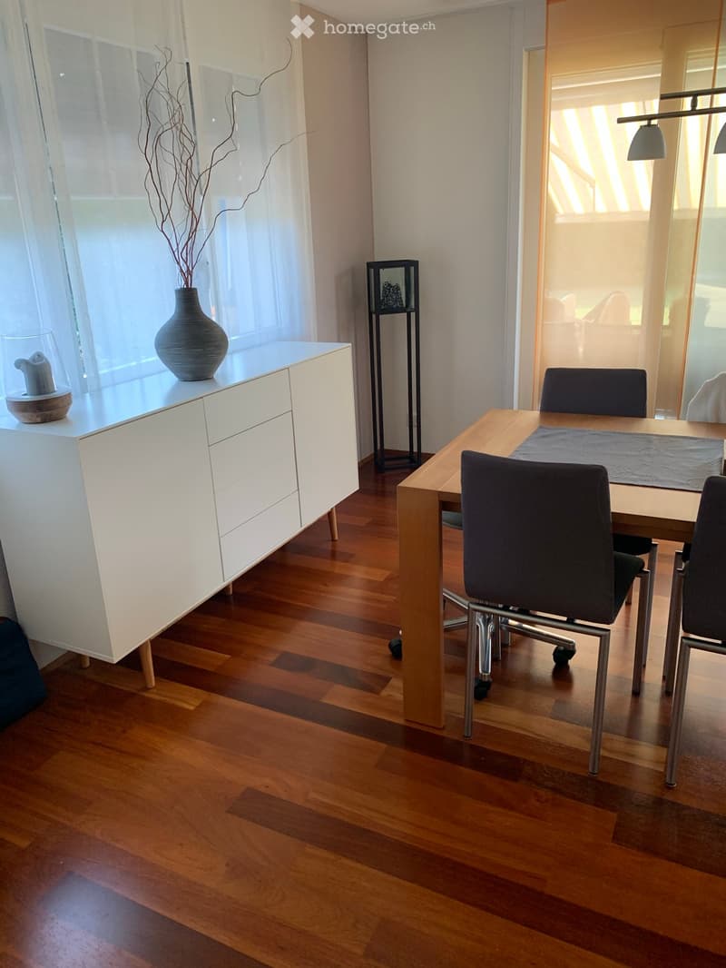 Dining area with wooden floor, white cabinet, wooden table, chairs, vase on cabinet, and a decorative shelf.