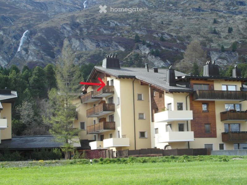 Apartment building with balconies, located in front of a mountain with a waterfall