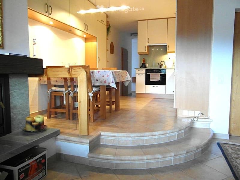 Open-plan living and dining area with a fireplace, dining table with chairs, and a modern kitchen with cabinets and appliances.