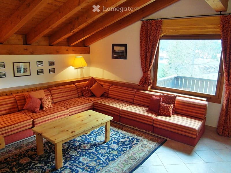 Cozy living room with exposed wooden beams, large window with view, sectional sofa, coffee table, floor lamp, and decorative picture frames.