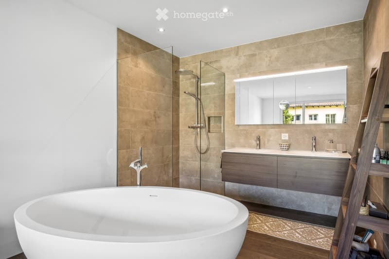 Bathroom. Modern bathroom with a freestanding bathtub, glass-enclosed shower, double sink vanity with wooden cabinets, large mirror with built-in lighting, and a small shelf with toiletries.