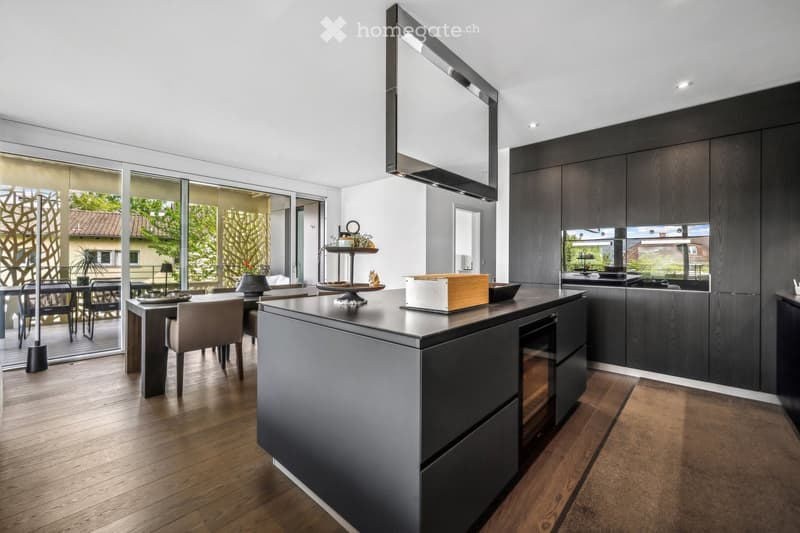 Kitchen. Modern kitchen with dark wood cabinets, a central island, and a dining area with chairs and a table. The space features a sleek design with a large window offering a view of the outdoor area.