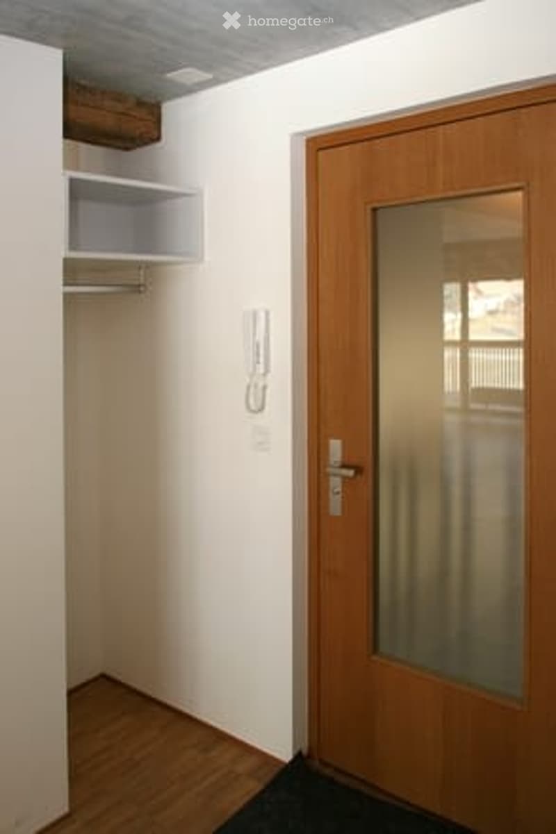 Empty room with light-colored walls, wooden floor, built-in closet with shelves, and a wooden door with a frosted glass panel.