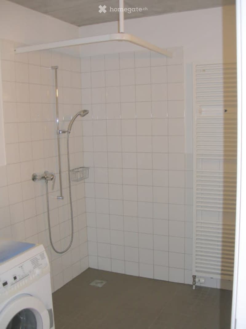 Clean, modern bathroom with white tiled walls, a shower, a radiator, and a washing machine.