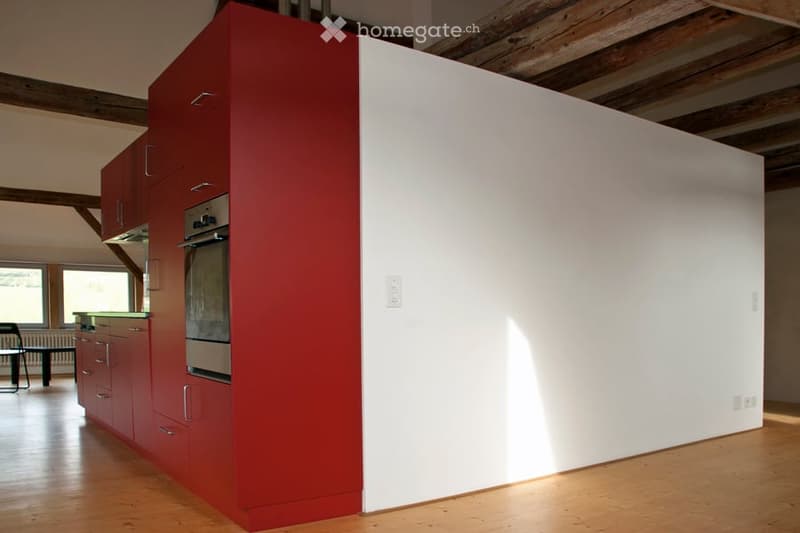 Modern kitchen with red and white cabinets, stainless steel oven, and wooden flooring.