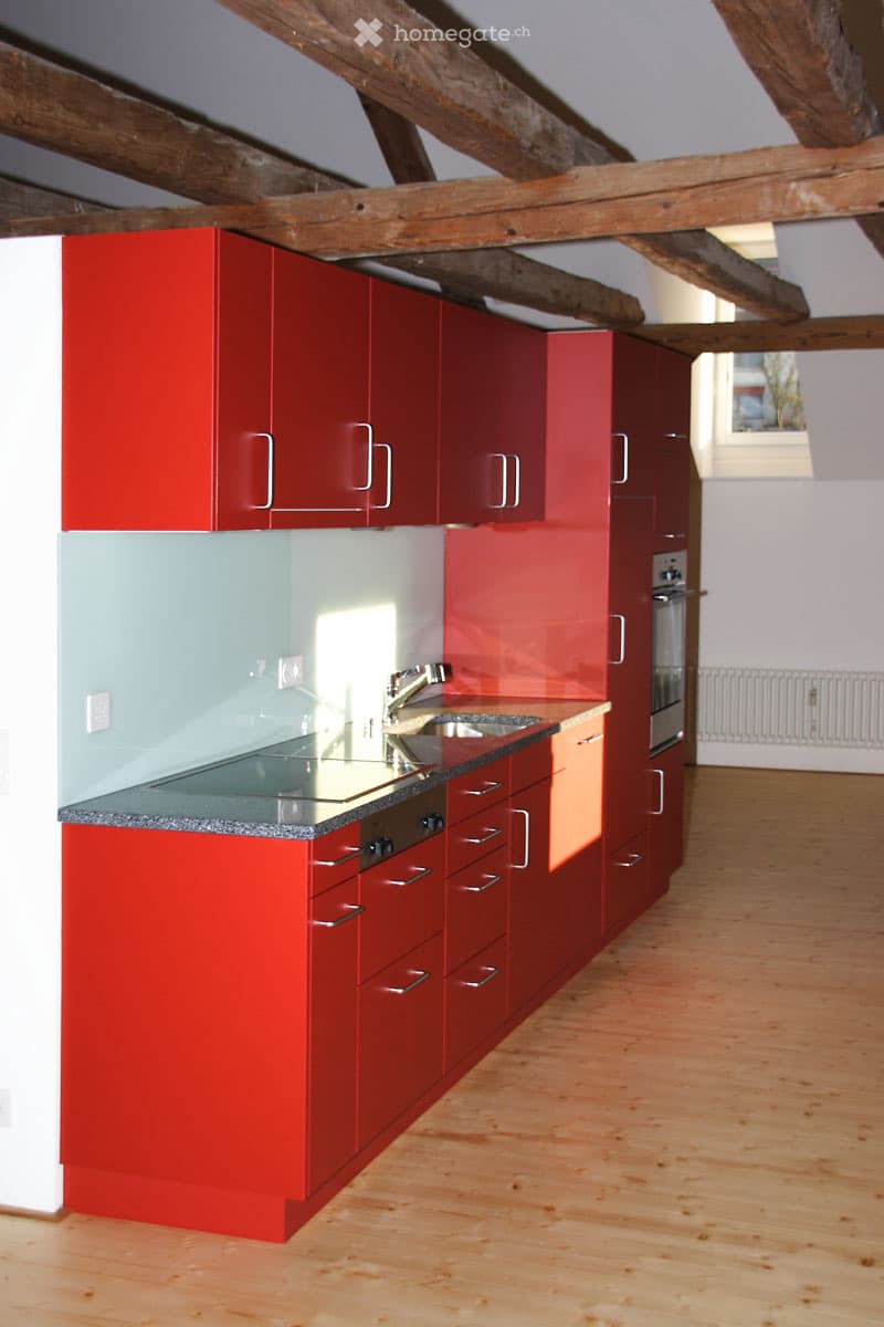 Modern kitchen with red cabinets, stainless steel sink, and wooden flooring.