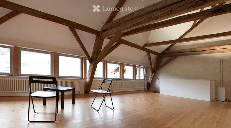 Bright, open room with wooden beams and large windows, featuring a small table and two chairs.