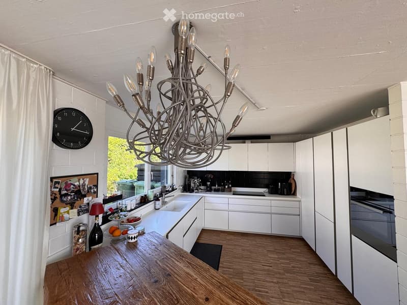Modern kitchen with white cabinets, wooden countertop, and a large chandelier.