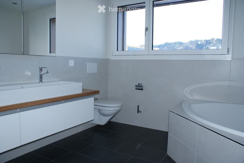 Modern bathroom with a white sink, faucet, toilet, bathtub, and large windows offering a scenic view.