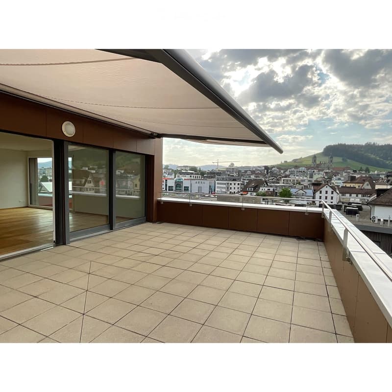 Spacious balcony with tiled floor, glass sliding doors leading to interior, and a panoramic city view under a partly cloudy sky.