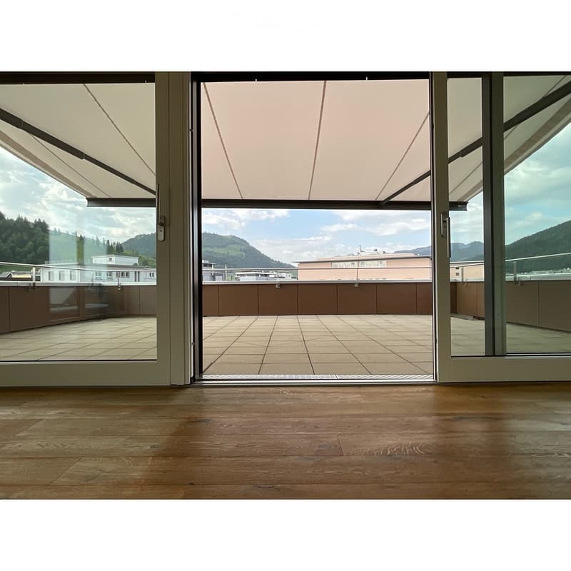 Empty room with wooden flooring and large sliding glass doors leading to a tiled balcony with a scenic mountain view.