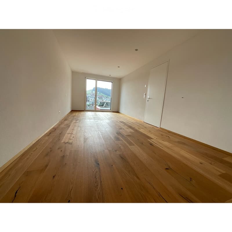 Empty room with wooden flooring, white walls, and a large sliding glass door leading to a scenic view.