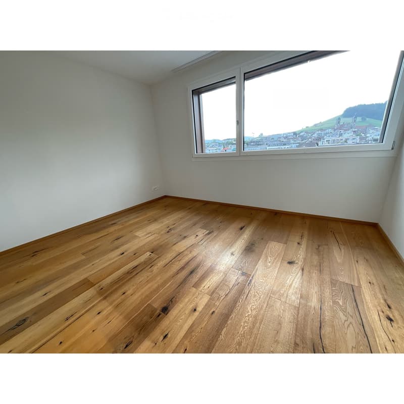 Empty room with wooden flooring and large windows offering a scenic view.