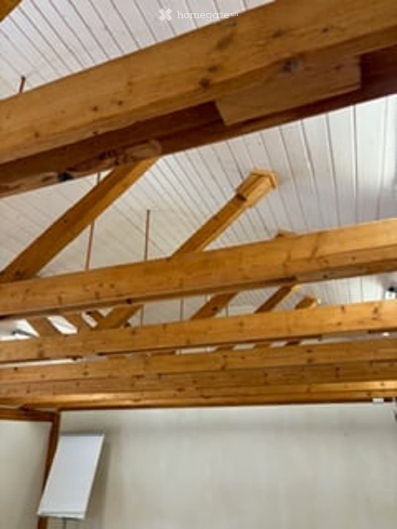 An unfurnished room with exposed wooden beams on the ceiling and white walls. The room appears to be a simple, unfinished space with no furniture or equipment.