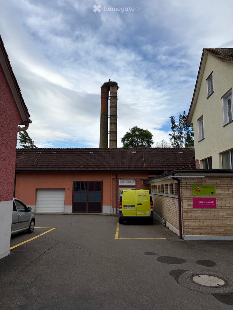 A multi-story building with a tiled roof, a chimney, and a garage entrance. A yellow van is parked in front, and there are signs directing to 'kleibundschrift' and 'LKK Elektro GmbH'.
