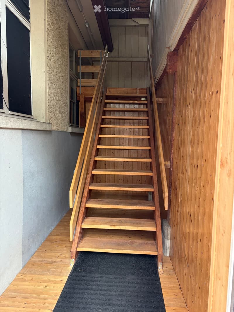 Wooden staircase with metal railings, black runner, wooden walls, and a window on the left side.