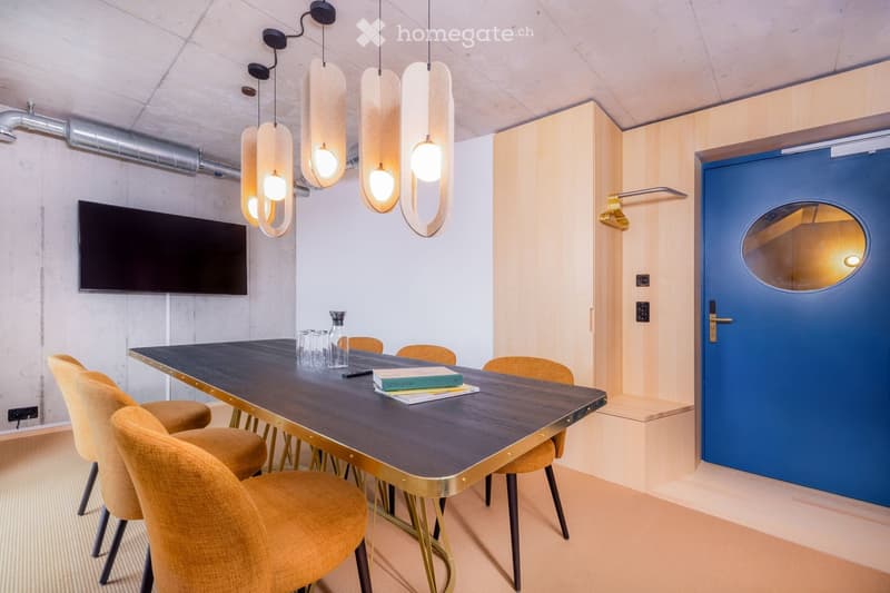 Modern, minimalist room with a dark wooden table, yellow chairs, pendant lights, and a television mounted on the wall.