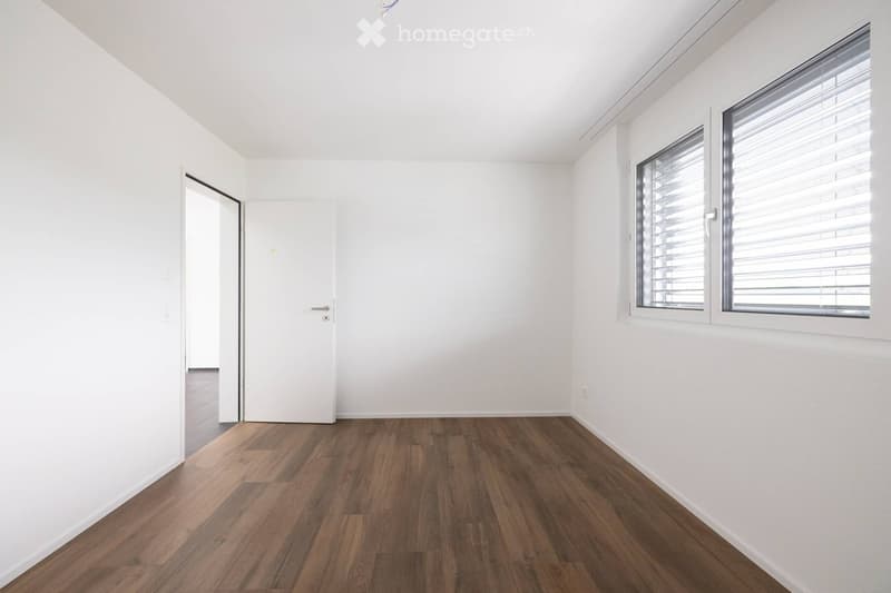 Empty room with white walls, wooden flooring, and large windows with blinds. No furniture or equipment present.